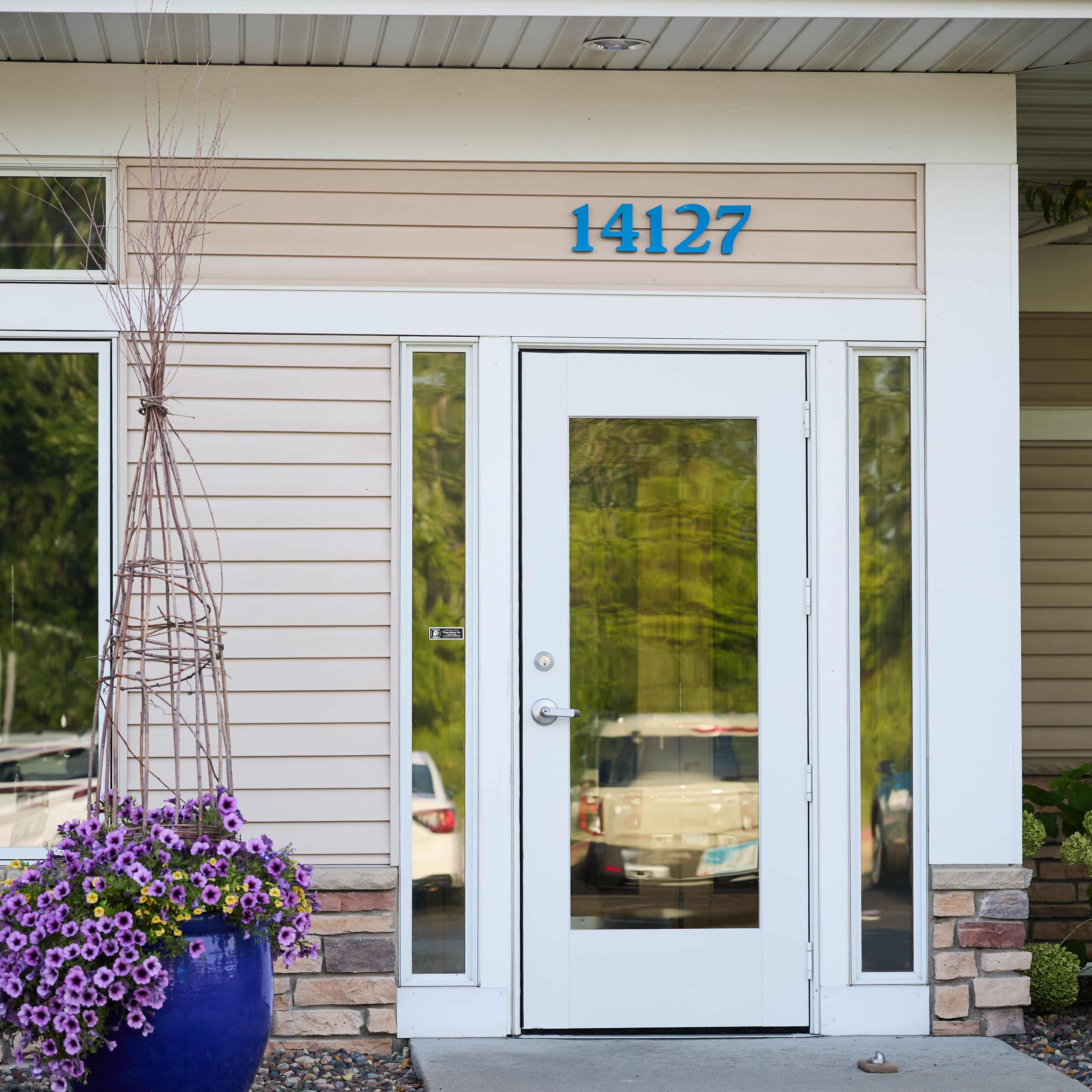 Front entrance of a house with blue address numbers 14127, glass door, and a blue pot of purple flowers on the left.